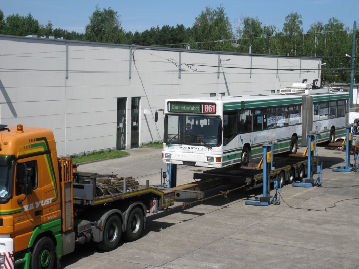 Der LKW-Tieflader fährt unter den angehobenen Gelenkobus.