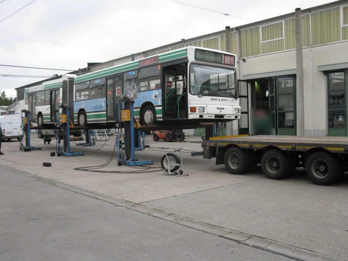 Der LKW-Tieflader fährt unter den angehobenen Gelenkobus.
